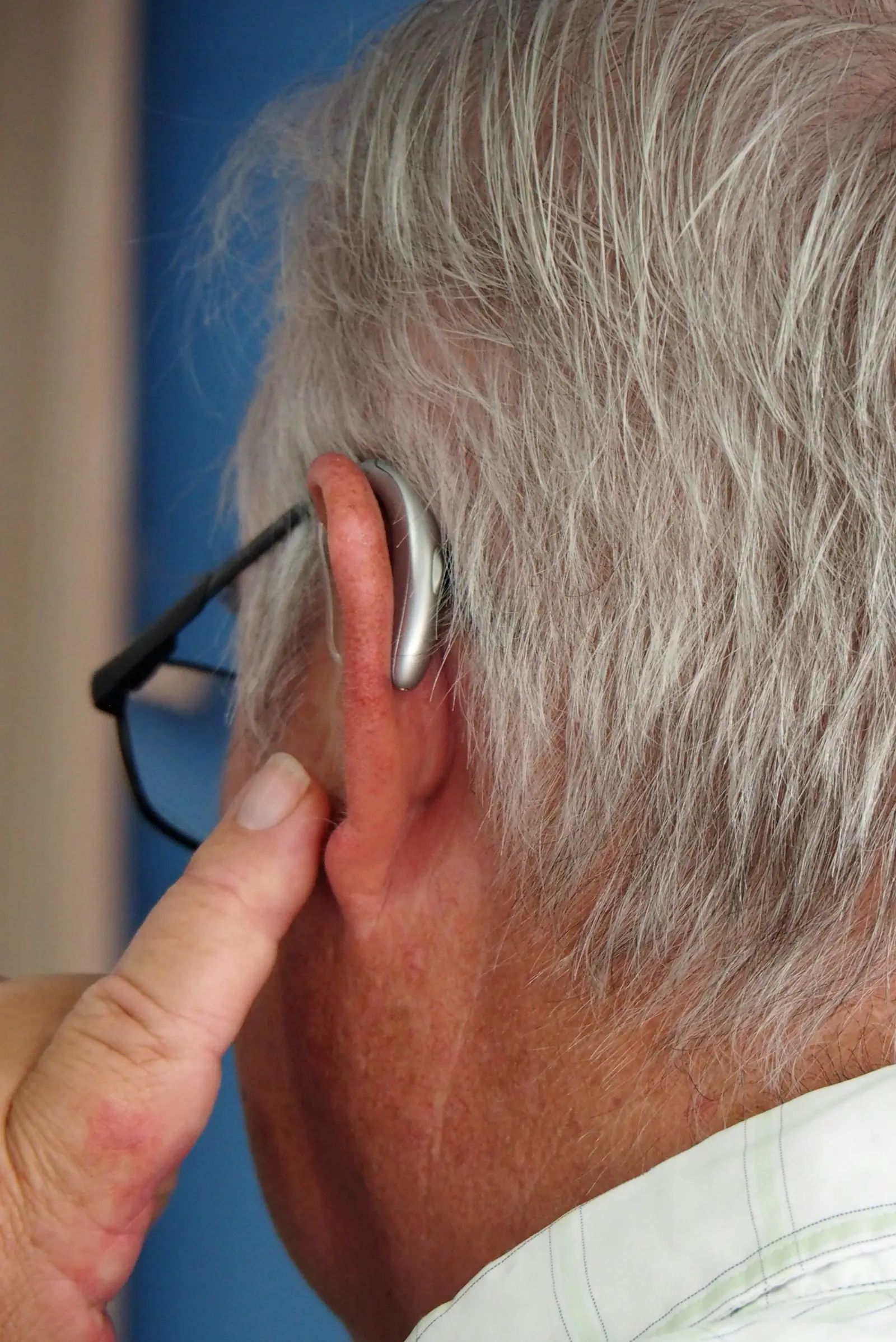 Audífono discreto colocado tras la oreja de un hombre mayor que también lleva gafas