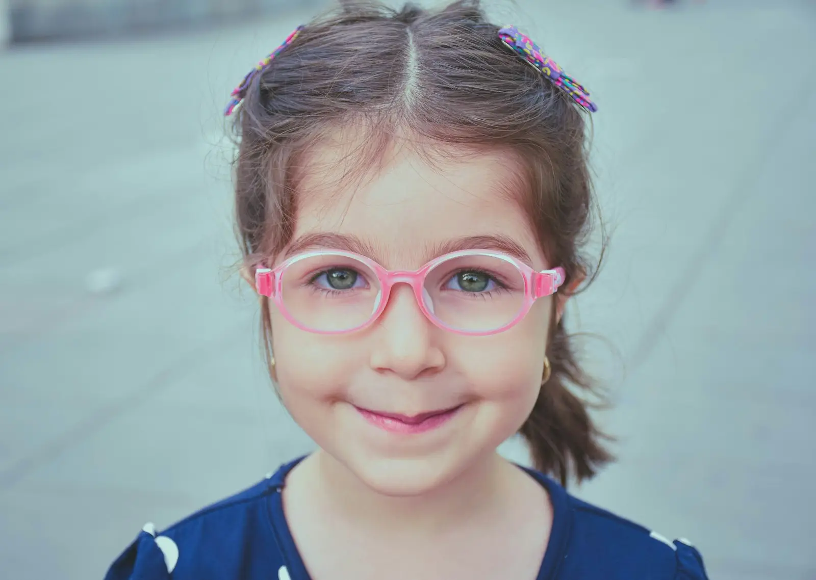 Niña de unos cinco años con gafas de montura rosa flexible, sonriendo en la calle
