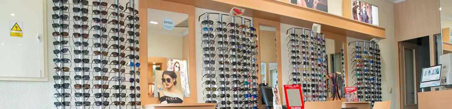 Paneles de pared de la tienda con hileras de monturas y gafas de sol colgadas, y espejos entre ellos