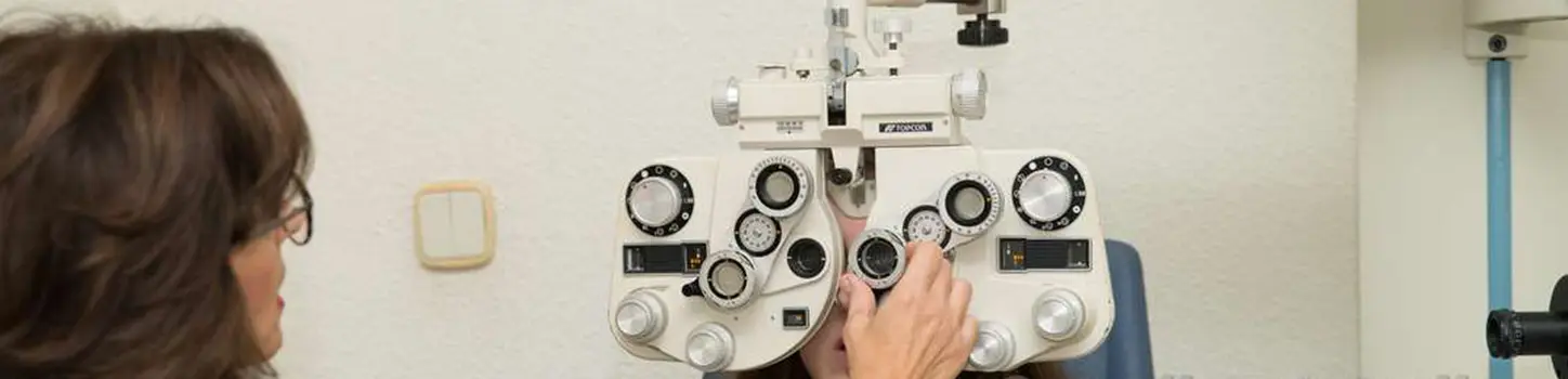 Optometrista sentada junto a un paciente que mira a través del foróptero mientras ella gira uno de los mandos
